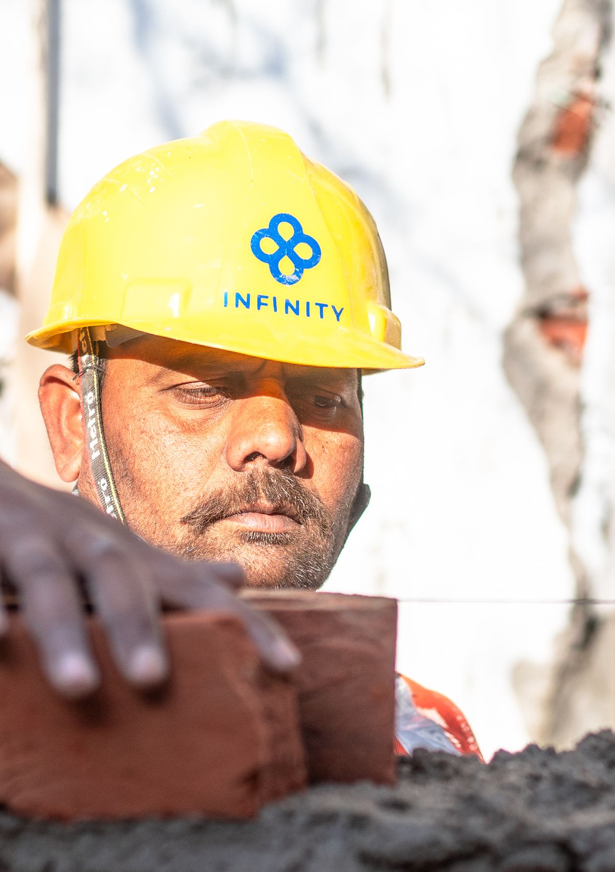 Indian mason in a hard hat laying brick at a construction site